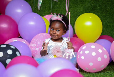 little girl with princess crown enjoying a birthday party surrounded by balloons.
