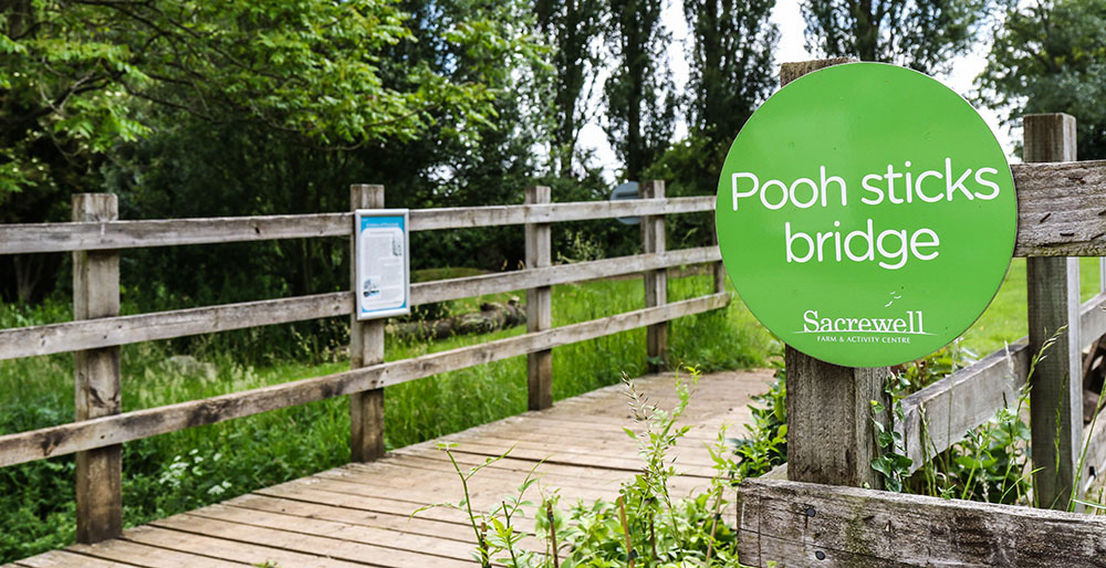 pooh sticks bridge at sacrewell. wooden bridge with signage, green grass and trees in background.